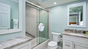 Une salle de bain moderne avec une douche à parois de verre, des toilettes blanches et un comptoir en marbre.