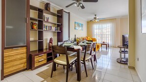 A dining area with a wooden table set for four, surrounded by chairs. There are ceiling fans, a bookshelf, and a television on a stand. - TERRAZAS DEL DUQUE II COSTA ADEJE (Costa Adeje)