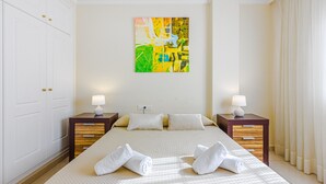 A hotel room with a large bed, two bedside tables, a painting on the wall, and a window with curtains. - TERRAZAS DEL DUQUE II COSTA ADEJE (Costa Adeje)