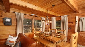 L’intérieur est en bois et comprend une table à manger, des bancs et des chaises. Il y a une horloge au mur et une fenêtre avec des rideaux.