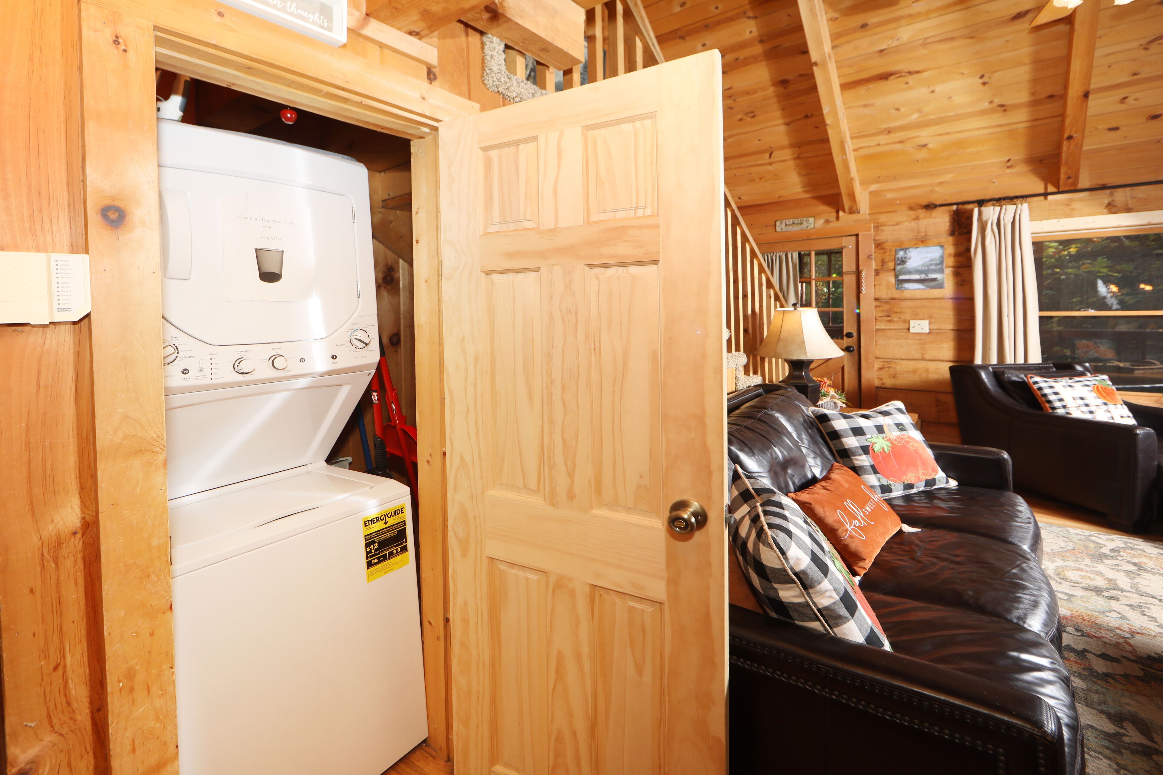 A laundry room with a washing machine and dryer, a wooden door, and a living area with a leather couch and pillows.