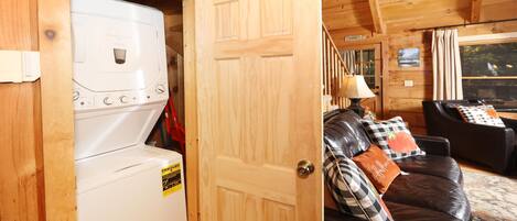A laundry room with a washing machine and dryer, a wooden door, and a living area with a leather couch and pillows.