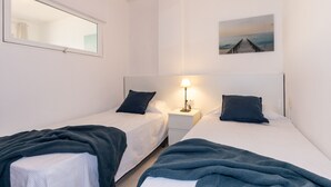 Une chambre double avec deux lits, une table de chevet avec une lampe, une fenêtre et un tableau au mur.