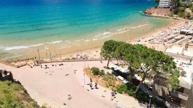 Une plage avec une promenade dallée, des parasols et une vue sur la mer et les montagnes.