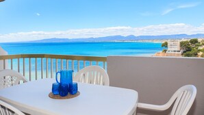 Un balcon avec une table et des chaises, offrant une vue sur la côte et les montagnes au loin.