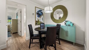 A dining area with a round table, four chairs, a teal cabinet, and a wall-mounted mirror. - Newly Renovated Partial Beach View 1 bed, 1 bath at Sanibel Moorings #141 (Sanibel)
