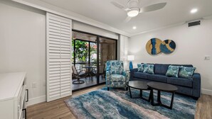 A modern living room with a blue sofa, two side tables, a patterned rug, and a ceiling fan. - Newly Renovated Partial Beach View 1 bed, 1 bath at Sanibel Moorings #141 (Sanibel)