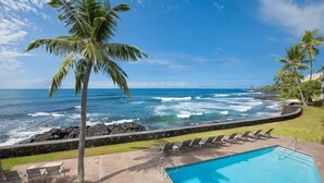 Ein Poolbereich mit Blick auf das Meer, Palmen und Liegestühle.