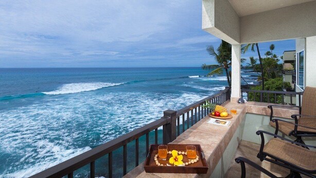 Ein Balkon mit Blick aufs Meer, ein Tablett mit Getränken und Obst sowie ein Stuhl.
