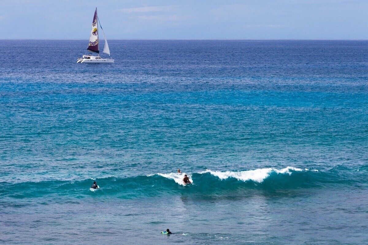 Un voilier sur une mer calme, avec des surfeurs dans l’eau.