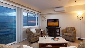 Ein Wohnzimmer mit großem Fenster zum Meer, einem Fernseher und zwei gemusterten Sesseln.