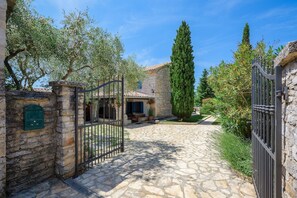 A stone pathway leading to a stone building with a metal gate, surrounded by trees and greenery. - Casa Biguli (Radici)