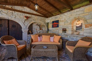 A stone-walled room with a sofa and two wicker chairs, a wooden ceiling, and a wall-mounted light fixture. - Casa Biguli (Radici)