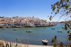 Uma vila costeira com edifícios à beira-mar, barcos na água e céu claro.