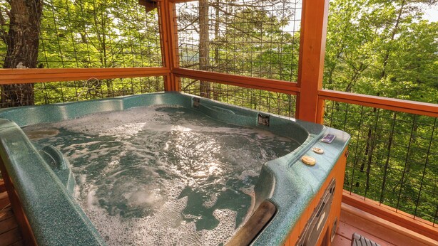 Ein Whirlpool mit Holzterrasse und Blick auf einen Wald durch ein Drahtgeflecht.