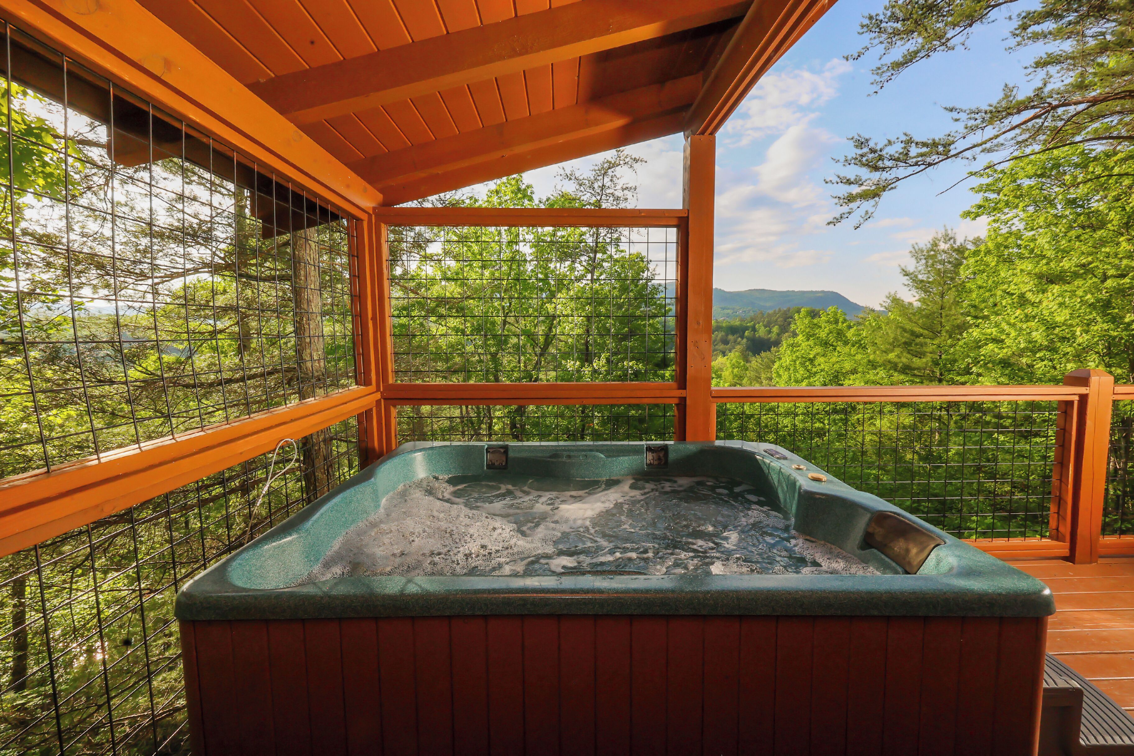 A hot tub on a wooden deck with a view of trees and mountains.