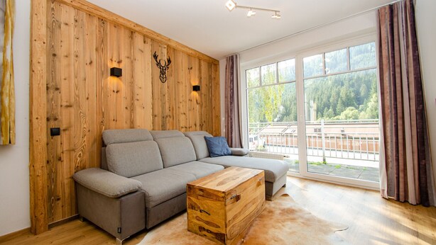 Un salon moderne avec un canapé d’angle, un mur d’accent en bois, de grandes fenêtres et une commode en bois.
