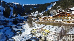 Un village de montagne enneigé, avec ses bâtiments traditionnels en bois, un ciel dégagé et une vue imprenable sur les montagnes environnantes.