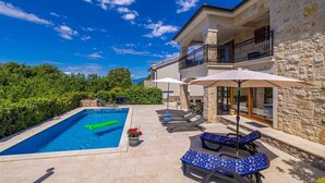 A pool area with lounge chairs and umbrellas, a stone building with a balcony, and a clear blue sky. - Holiday house OBZOVA with private heated pool (Ljutići)