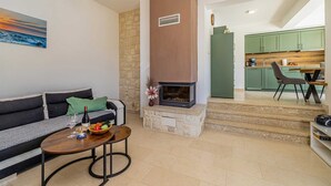 A living room with a sofa, coffee table, and a fireplace. There is a kitchen visible in the background. - Holiday house OBZOVA with private heated pool (Ljutići)