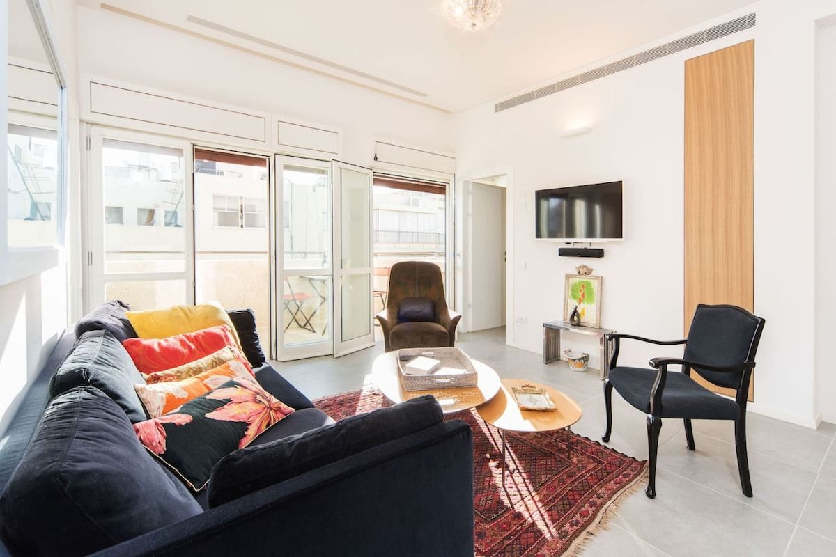 Ein modernes Wohnzimmer mit einer Couch, Sesseln, einem Couchtisch und einem an der Wand befestigten Fernseher.