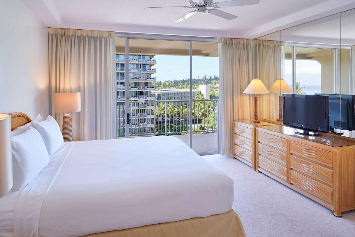 Ein Hotelzimmer mit einem großen Bett, einem Fernseher auf einer Holzkommode und einem Balkon mit Blick auf die Stadt.