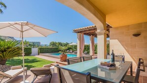 Une terrasse extérieure avec une table en verre, des chaises et une piscine en arrière-plan.
