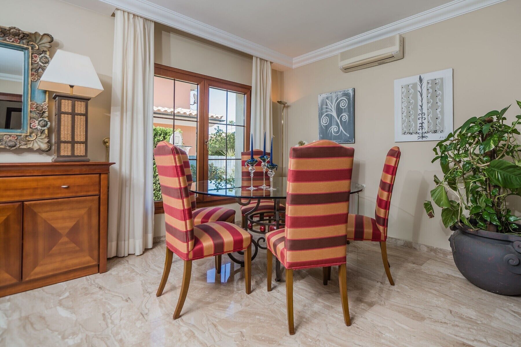 Un coin repas avec des chaises à rayures, une table en verre et une plante en pot.