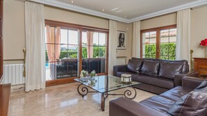 Un salon spacieux avec une table basse en verre, un canapé en cuir et de grandes fenêtres donnant sur un paysage verdoyant.