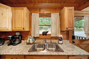 A kitchen with wooden cabinets, a double sink, a coffee maker, and a window with curtains. - Private, Hot Tub, Mtn View, FREE Amenities, 5 miles from Pigeon Forge!! (Sevierville)