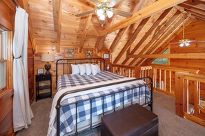 A wooden cabin bedroom with a bed, a nightstand, a lamp, a ceiling fan, and a window. - Private, Hot Tub, Mtn View, FREE Amenities, 5 miles from Pigeon Forge!! (Sevierville)