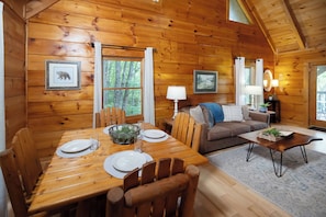 A wooden cabin interior with a dining table set for two, a sofa, and a coffee table. - Private, Hot Tub, Mtn View, FREE Amenities, 5 miles from Pigeon Forge!! (Sevierville)