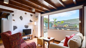 Una sala de estar con televisor, sofá y vista a un jardín a través de un ventanal grande.