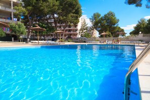 A swimming pool with lounge chairs and umbrellas, surrounded by trees and a building with balconies. - Sea Views Apartment · AirCon · Pool · UHC PACIFIC 197 (Salou)