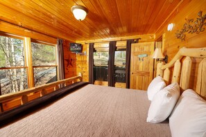 A wooden cabin room with a large bed, a television, and a window overlooking a forest. - Private, Beautiful Views! Pool Table, Hot Tub, Arcade Game! (Sevierville)