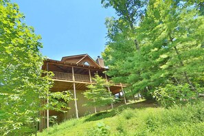 A wooden cabin with a balcony, surrounded by lush greenery. - Private, Beautiful Views! Pool Table, Hot Tub, Arcade Game! (Sevierville)