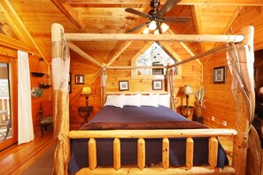 A wooden cabin interior with a bed, ceiling fan, and framed pictures on the walls.