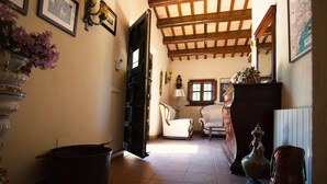Un pasillo con suelo de baldosas, una puerta negra, una silla blanca, un armario de madera y un jarrón con flores.