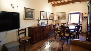 Una sala de estar con televisor, muebles de madera, una mesa de centro de vidrio y obras de arte en las paredes.