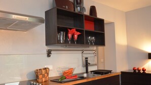 Une cuisine dotée d’un plan de travail noir, d’un four encastré et d’une étagère au-dessus du plan de travail, où sont rangés divers ustensiles de cuisine.