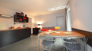 Une cuisine moderne avec des meubles de rangement aux couleurs sombres, une table à manger en bois et deux chaises en fil de métal.