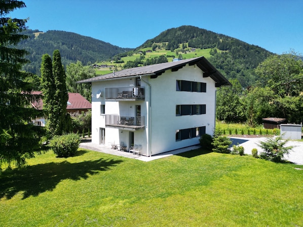 A two-story building with a balcony, surrounded by greenery and mountains.