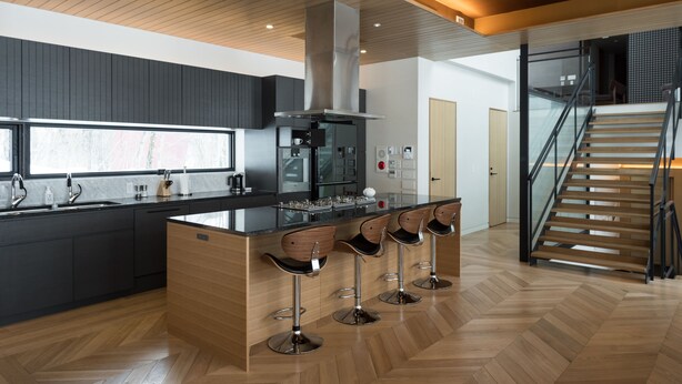 Una cocina moderna con una isla central, taburetes de bar y una escalera que lleva a un nivel superior.
