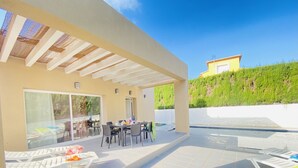 An outdoor patio with a covered dining area, lounge chairs, and a pool.