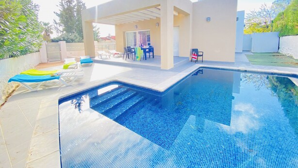 A modern outdoor pool area with lounge chairs, a covered seating area, and a clear view of the pool.