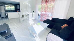 A modern living room with a black sofa, a white coffee table, and a dining area with a glass table and white chairs.
