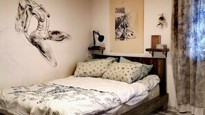 A bedroom with a wooden ceiling, a bed with patterned bedding, a wall mural, a desk with a lamp, and a patterned floor. - Helen and David's apartment,, Bird's nest" (Didube-Chugureti)