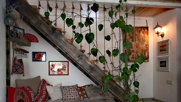 A cozy room with a wooden staircase, a sofa with patterned cushions, a potted plant, and wall art. - Helen and David's apartment,, Bird's nest" (Didube-Chugureti)