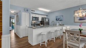 A modern kitchen with white cabinetry, a central island with bar stools, a stainless steel refrigerator, and a microwave.