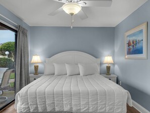 Une chambre à coucher avec un lit, deux tables de chevet avec des lampes, un ventilateur de plafond et un tableau au mur.